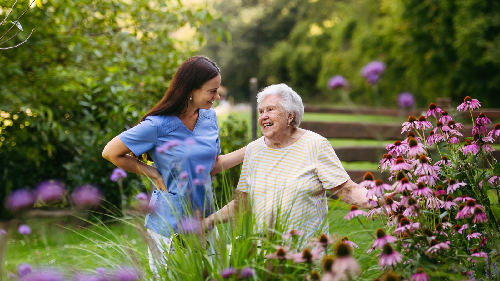 A Helen's Home Care caregiver walking with a senior woman through her garden