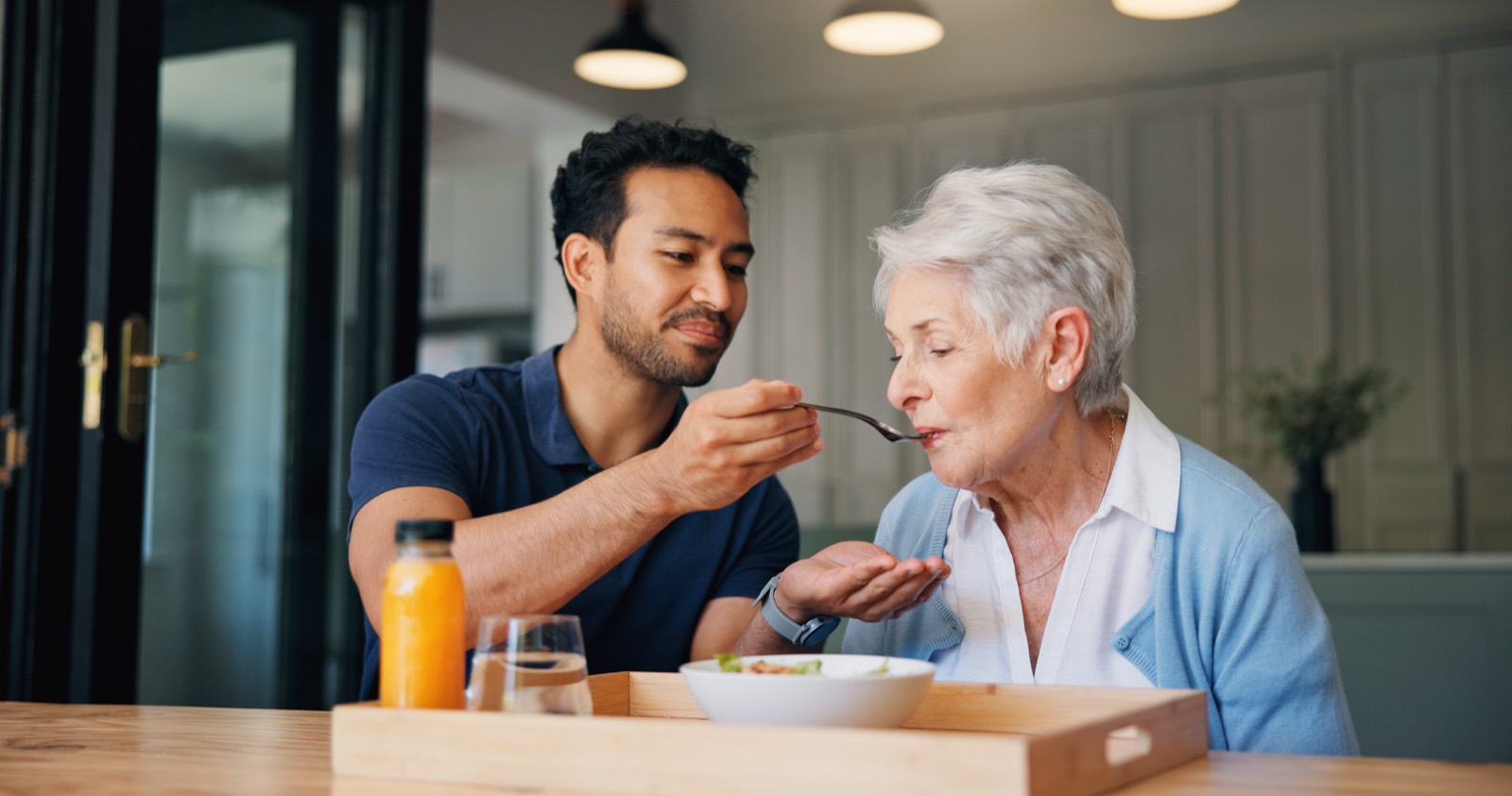 A Helen's Home Care caregiver helping a senior woman with a meal at home